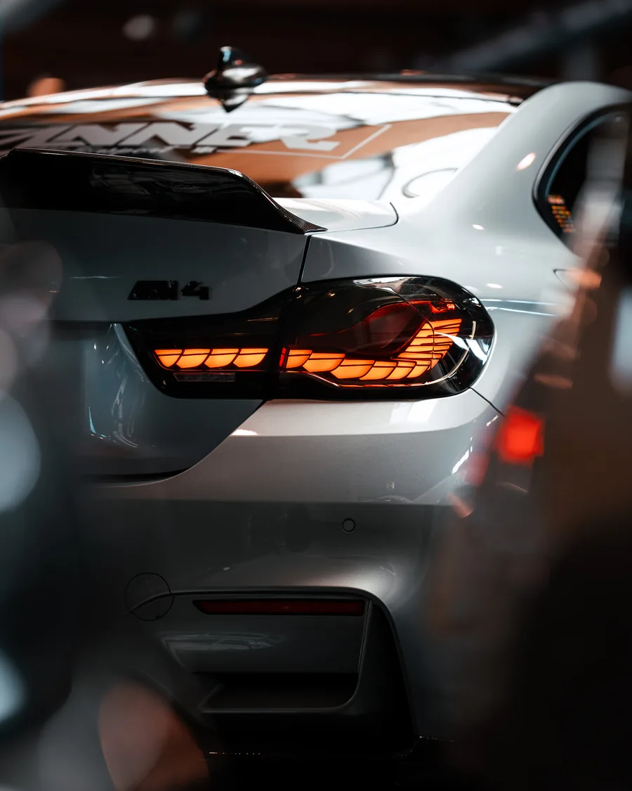 Heckpartie eines weißen BMW M4 mit leuchtender OLED-Rückleuchte im Halbdunkel – Automotive-Fotografie